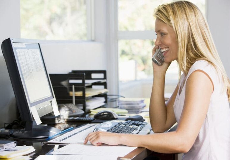 Woman in home office with computer using telephone smiling